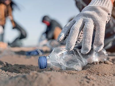 hand picking up plastic bottle during beach cleanup